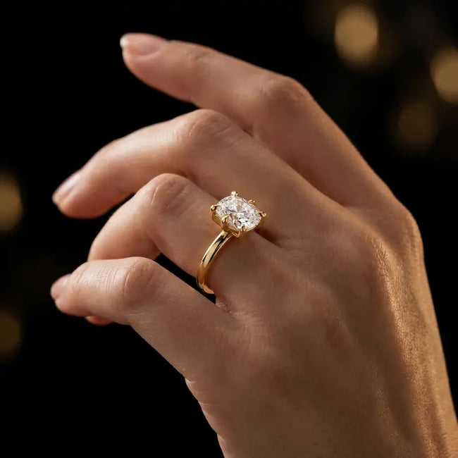 1.5 carat cushion cut diamond solitaire engagement ring in an 18kt yellow gold 6 claw setting worn on a hand, by TJ Diamond