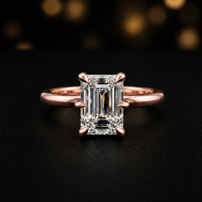 Front view of a 1.5 carat emerald cut diamond solitaire engagement ring in an 18kt rose gold 6 claw setting by TJ Diamond