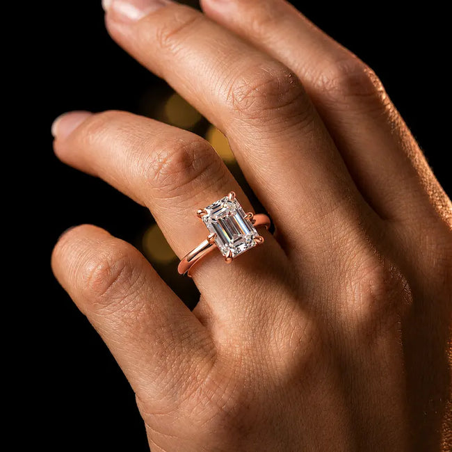 1.5 carat emerald cut diamond solitaire engagement ring in an 18kt rose gold 6 claw setting worn on a hand, by TJ Diamond