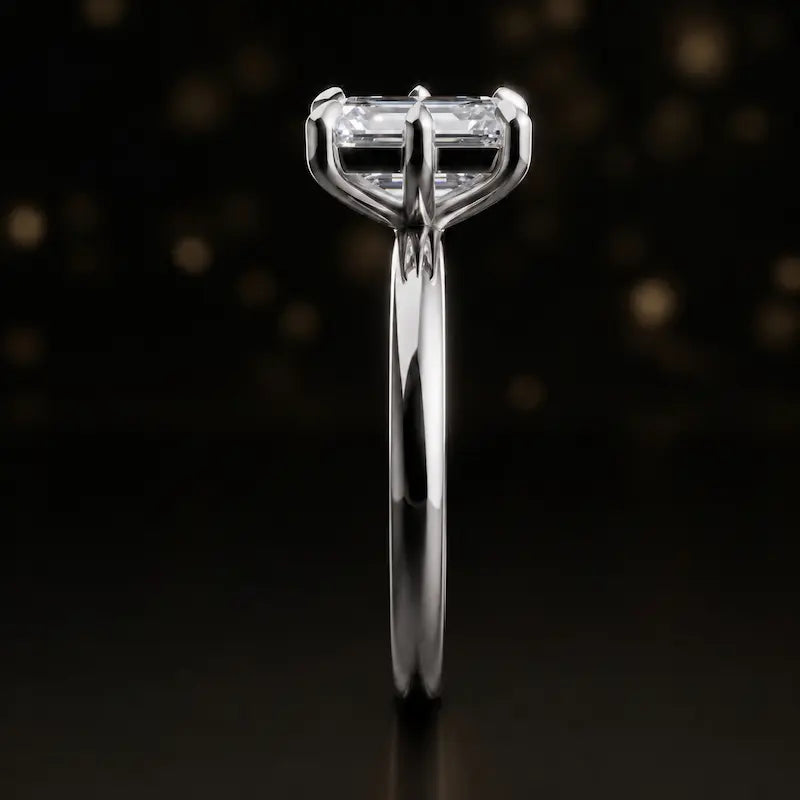 Side profile of a 1.5 carat emerald cut diamond solitaire engagement ring showing the cathedral setting and 18kt white gold band by TJ Diamond