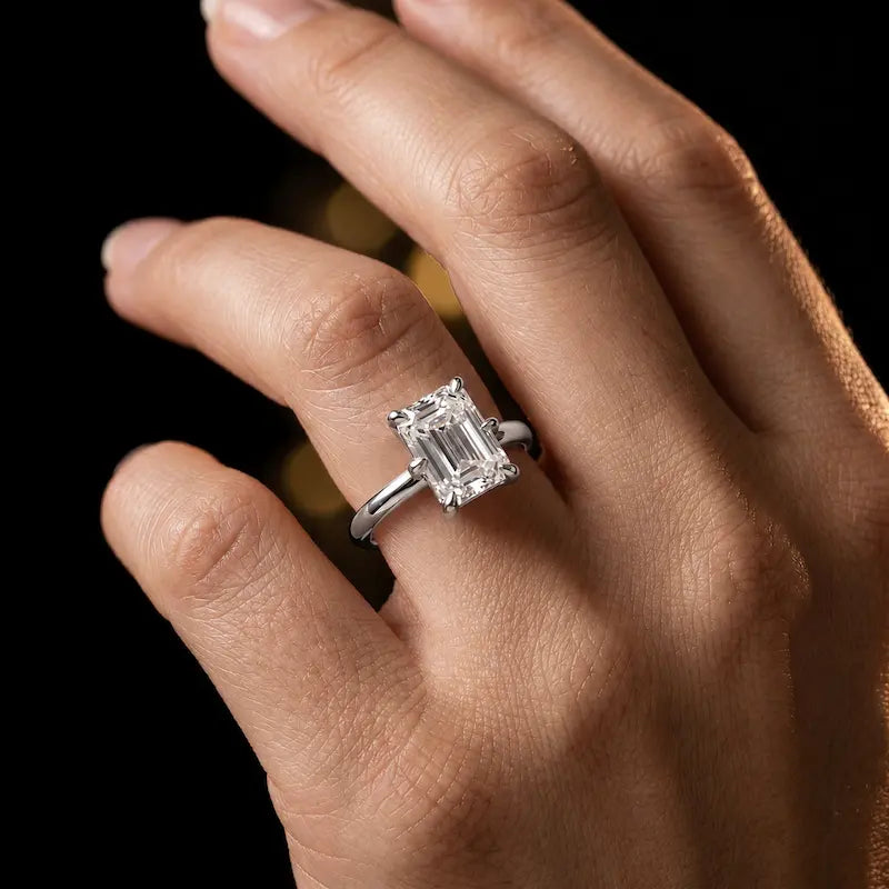 1.5 carat emerald cut diamond solitaire engagement ring in an 18kt white gold 6 claw setting worn on a hand, by TJ Diamond