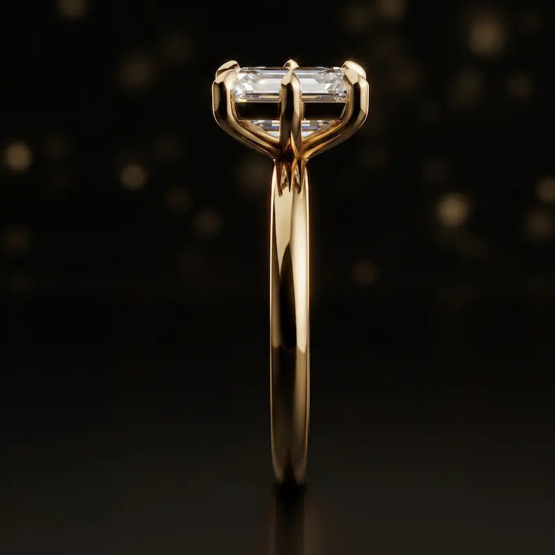 Side profile of a 1.5 carat emerald cut diamond solitaire engagement ring showing the cathedral setting and 18kt yellow gold band by TJ Diamond