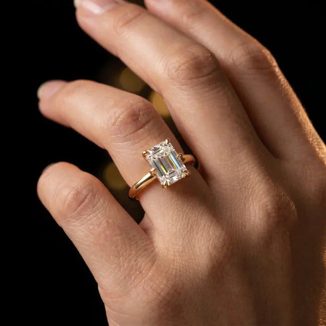 1.5 carat emerald cut diamond solitaire engagement ring in an 18kt yellow gold 6 claw setting worn on a hand, by TJ Diamond
