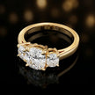 Angled view of a cushion-cut lab-grown diamond trilogy engagement ring in polished 18ct yellow gold.