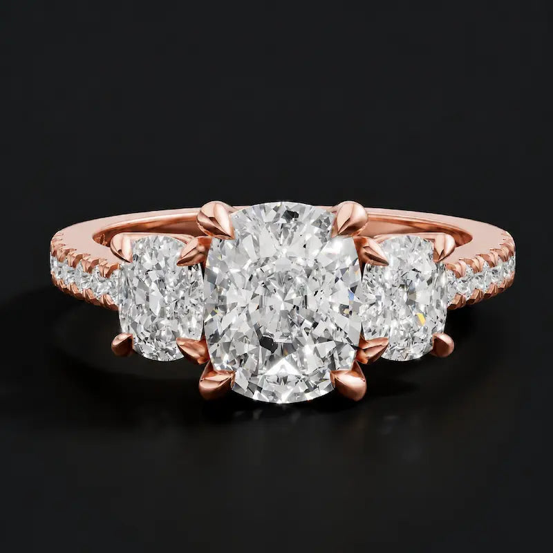 Front view of a cushion cut three-stone diamond engagement ring in 18kt rose gold, with a cushion cut centre stone, two cushion cut side stones, and diamond shoulders