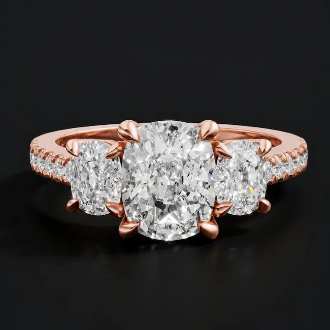 Front view of a cushion cut three-stone diamond engagement ring in 18kt rose gold, with a cushion cut centre stone, two cushion cut side stones, and diamond shoulders