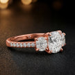 Side angle of a cushion cut three-stone diamond engagement ring in 18kt rose gold showing the trilogy setting and diamond shoulders