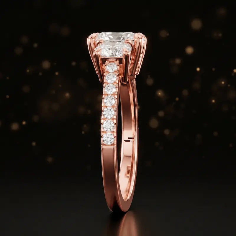 Side profile of a cushion cut three-stone diamond engagement ring in 18kt rose gold showing the band elevation and diamond shoulders