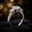 Angle view of a cushion cut three-stone diamond engagement ring in 18kt white gold, with a centre stone, two side stones, and diamond shoulders