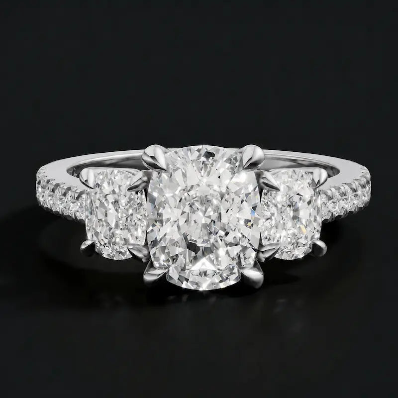 Front view of a cushion cut three-stone diamond engagement ring in 18kt white gold, with a cushion cut centre stone, two cushion cut side stones, and diamond shoulders