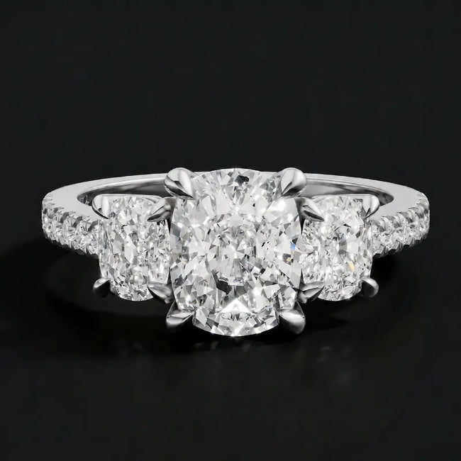 Front view of a cushion cut three-stone diamond engagement ring in 18kt white gold, with a cushion cut centre stone, two cushion cut side stones, and diamond shoulders