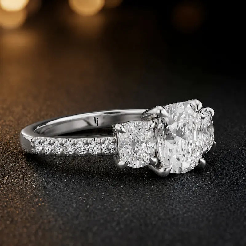 Side view of a cushion cut three-stone diamond engagement ring in 18kt white gold showing the trilogy setting and diamond shoulders