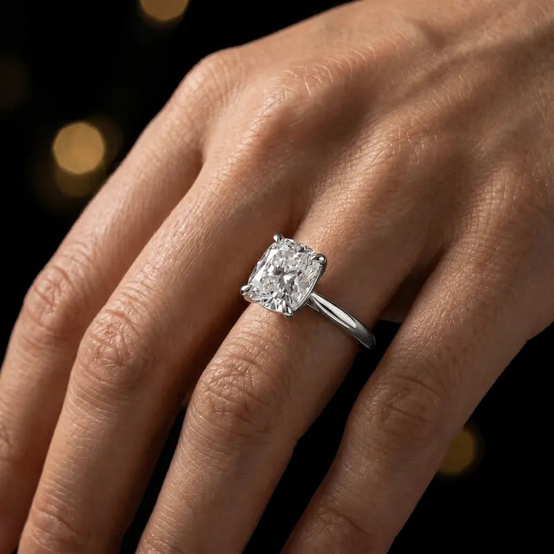 1.5 carat cushion cut diamond solitaire engagement ring in an 18kt white gold 4 claw setting worn on a hand, by TJ Diamond