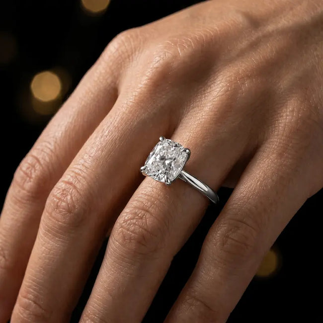 1.5 carat cushion cut diamond solitaire engagement ring in an 18kt white gold 4 claw setting worn on a hand, by TJ Diamond