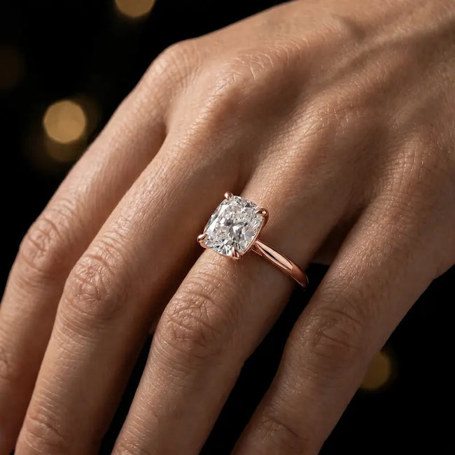 1.5 carat cushion cut diamond solitaire engagement ring in an 18kt rose gold 4 claw setting worn on a hand, by TJ Diamond