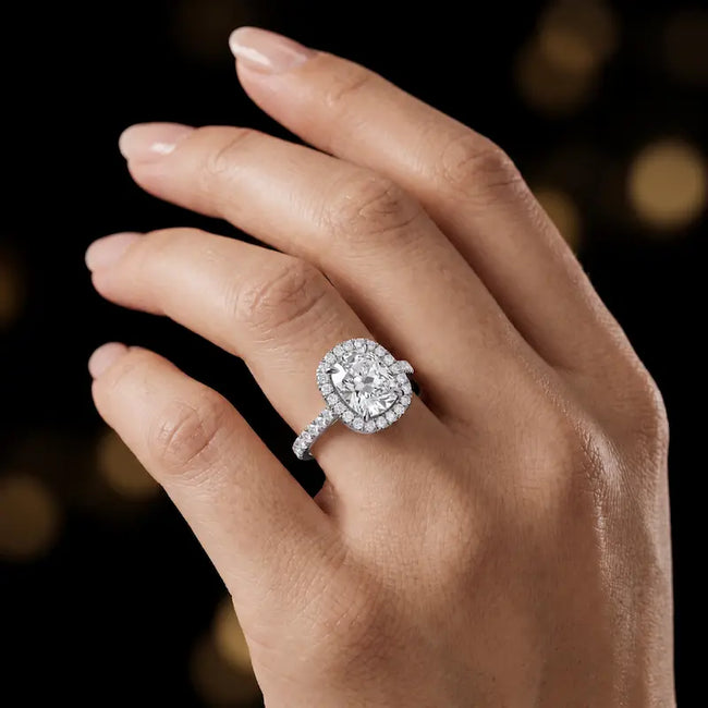 Cushion cut halo lab-grown diamond engagement ring worn on hand in 18kt white gold.