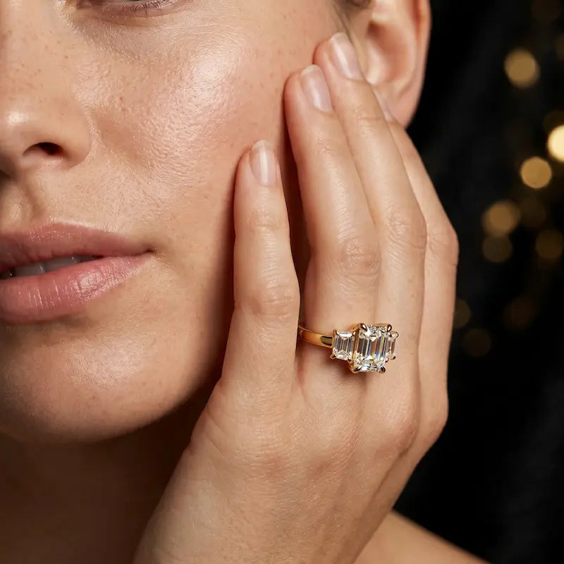 Model wearing an emerald-cut lab-grown diamond trilogy engagement ring handcrafted in 18kt yellow gold.