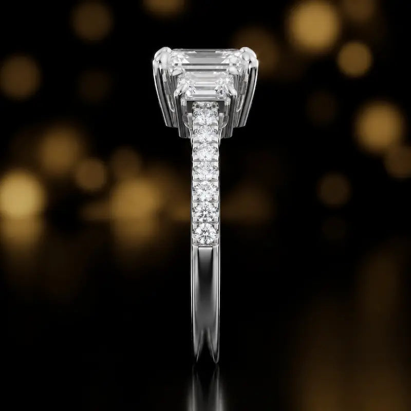 Side profile of an emerald cut three-stone lab-grown diamond engagement ring in 18kt white gold showing the diamond band