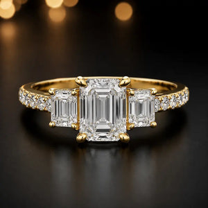 Front view of an emerald cut three-stone lab-grown diamond engagement ring in 18kt yellow gold with diamond shoulders