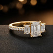 Side view of an emerald cut three-stone lab-grown diamond engagement ring in 18kt yellow gold with diamond shoulders