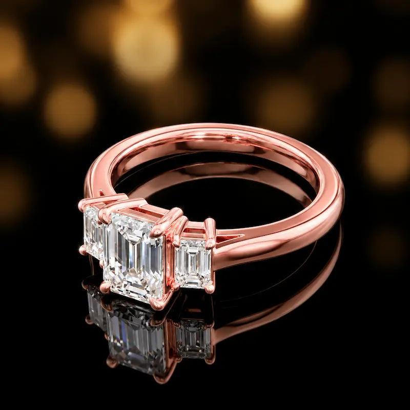 Side view of an emerald-cut three-stone lab-grown diamond engagement ring in 18ct rose gold, highlighting the elevated basket setting.