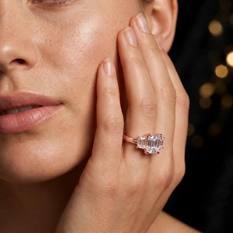 Model wearing an emerald-cut lab-grown diamond trilogy engagement ring in handcrafted 18ct rose gold.
