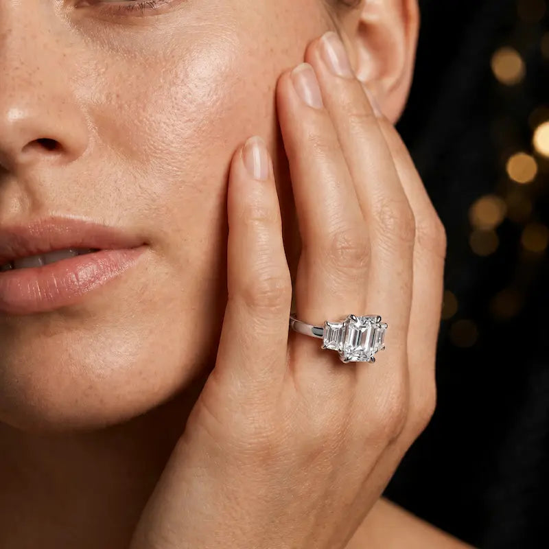 Model wearing an emerald-cut lab-grown diamond trilogy engagement ring handcrafted in 18ct white gold.