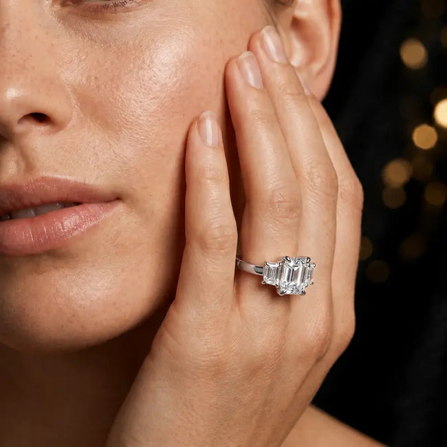 Model wearing an emerald-cut lab-grown diamond trilogy engagement ring handcrafted in 18ct white gold.