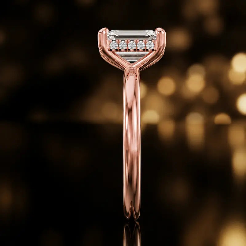 Side profile of 4-claw emerald cut engagement ring with hidden halo in 18kt rose gold