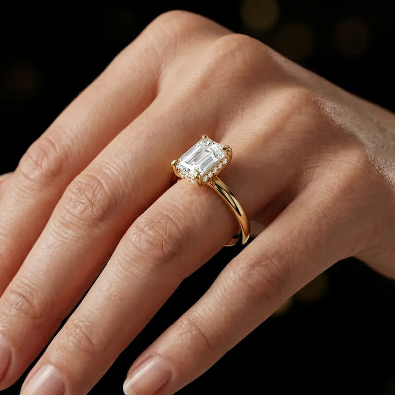 4-claw emerald cut engagement ring with hidden halo in 18kt yellow gold, worn on hand