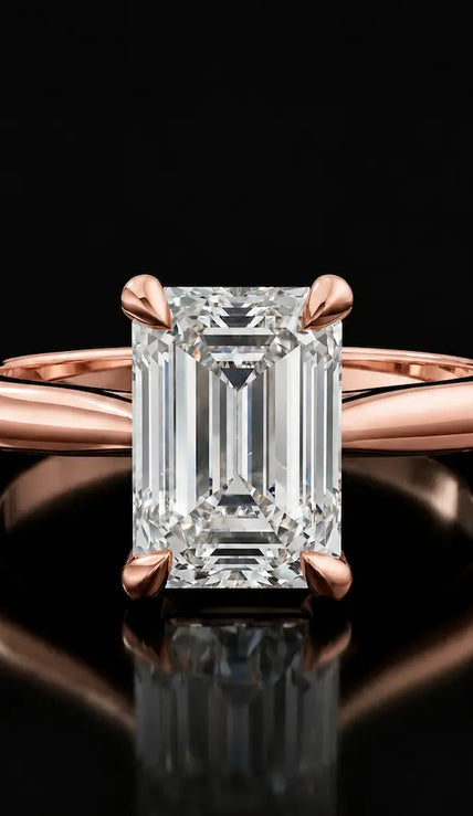 Front view of a 1.5 carat emerald cut diamond solitaire engagement ring in an 18kt rose gold 4 claw setting by TJ Diamond