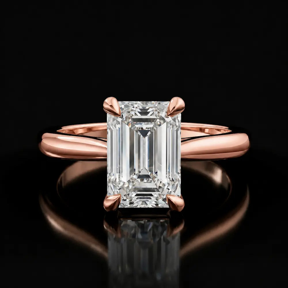 Front view of a 1.5 carat emerald cut diamond solitaire engagement ring in an 18kt rose gold 4 claw setting by TJ Diamond