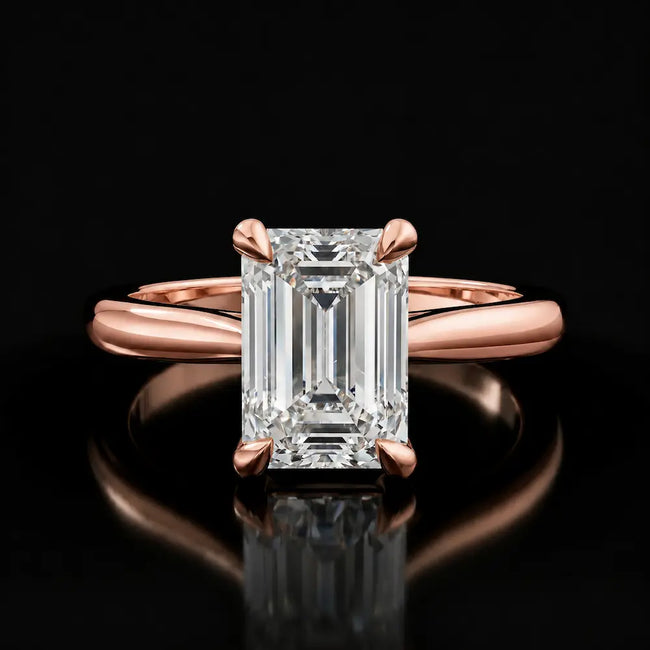 Front view of a 1.5 carat emerald cut diamond solitaire engagement ring in an 18kt rose gold 4 claw setting by TJ Diamond