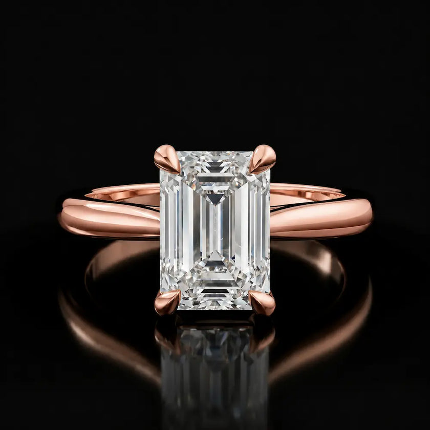 Front view of a 1.5 carat emerald cut diamond solitaire engagement ring in an 18kt rose gold 4 claw setting by TJ Diamond