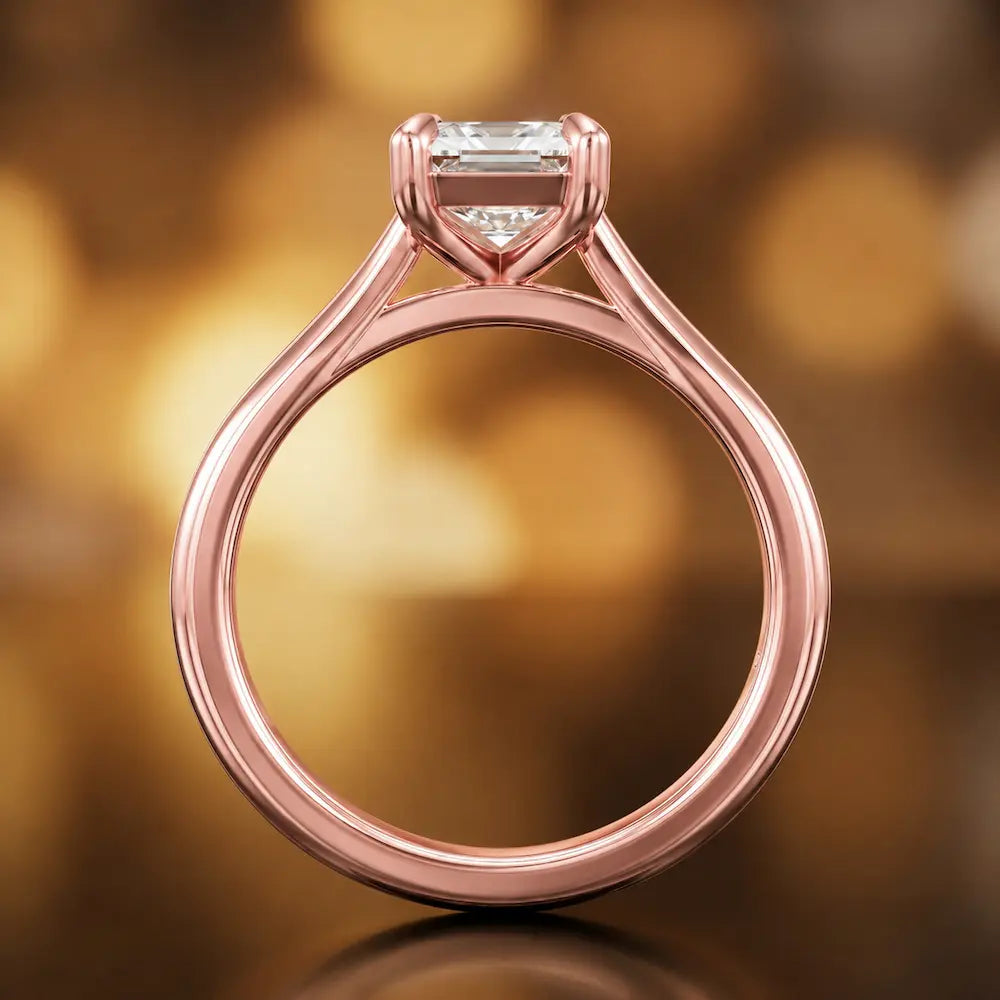 Front-on view of a 1.5 carat emerald cut diamond solitaire engagement ring showing the full 18kt rose gold band and 4 claw cathedral setting by TJ Diamond