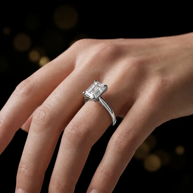 1.5 carat emerald cut diamond solitaire engagement ring in an 18kt white gold 4 claw setting worn on a hand, by TJ Diamond