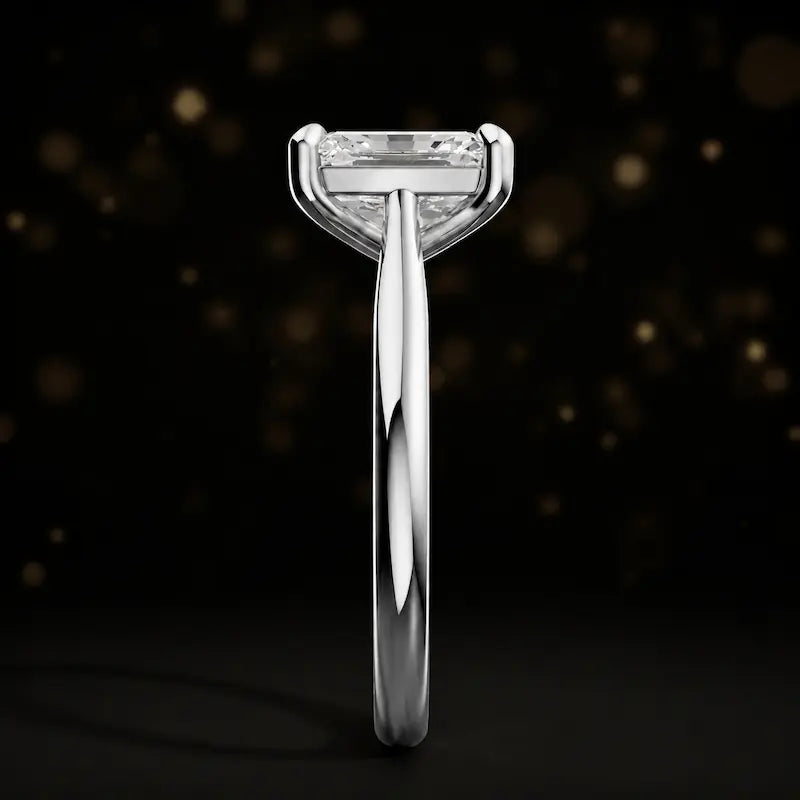 Side profile of a 1.5 carat emerald cut diamond solitaire engagement ring showing the cathedral setting and 18kt white gold band by TJ Diamond
