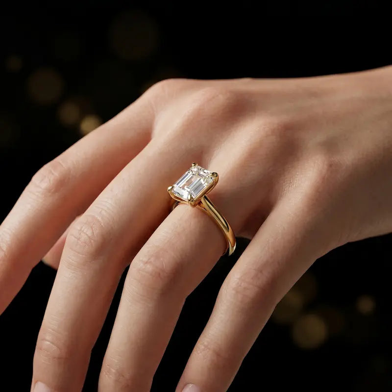 1.5 carat emerald cut diamond solitaire engagement ring in an 18kt yellow gold 4 claw setting worn on a hand, by TJ Diamond