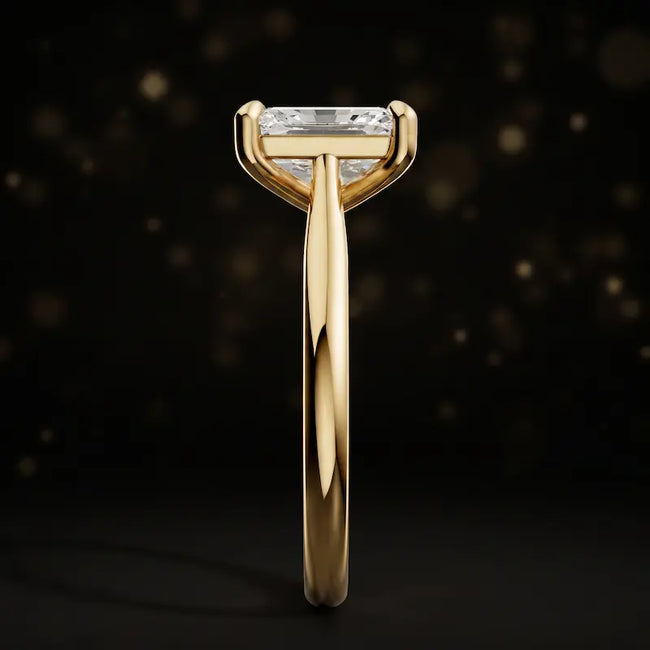 Side profile of a 1.5 carat emerald cut diamond solitaire engagement ring showing the cathedral setting and 18kt yellow gold band by TJ Diamond