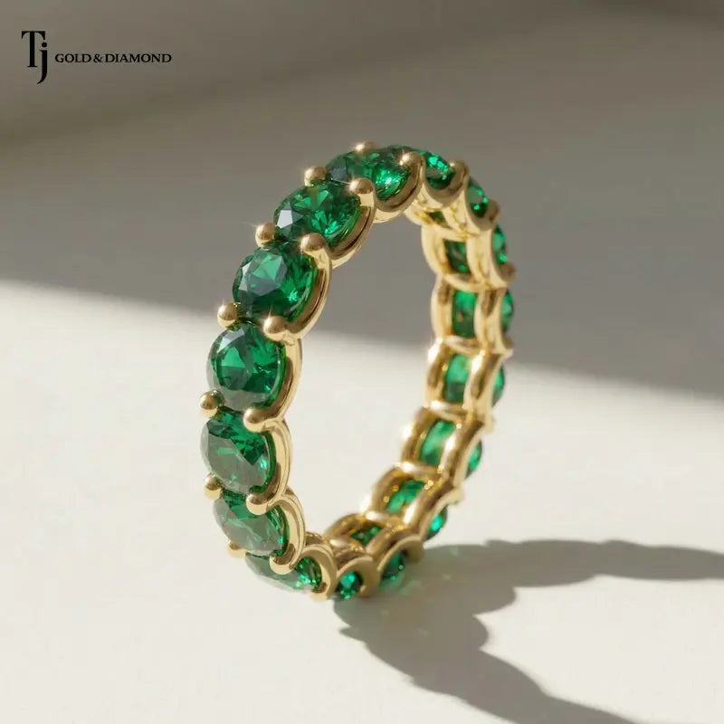Angled view of a created emerald full eternity ring in 18kt yellow gold with 1.5mm round brilliant lab-created emeralds.