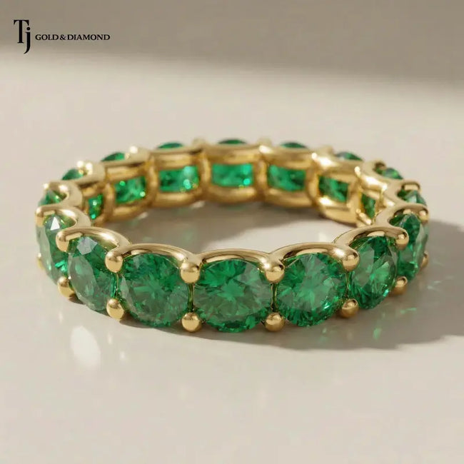 Created emerald full eternity ring in 18kt yellow gold featuring 1.5mm round brilliant lab-created emeralds in a shared prong setting.