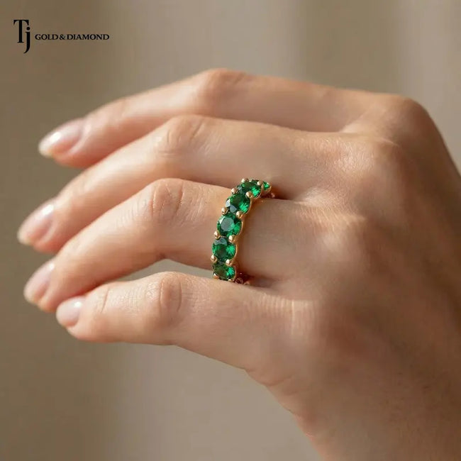 Created emerald full eternity ring in 18kt yellow gold with 1.5mm round brilliant lab-created emeralds worn on a hand.