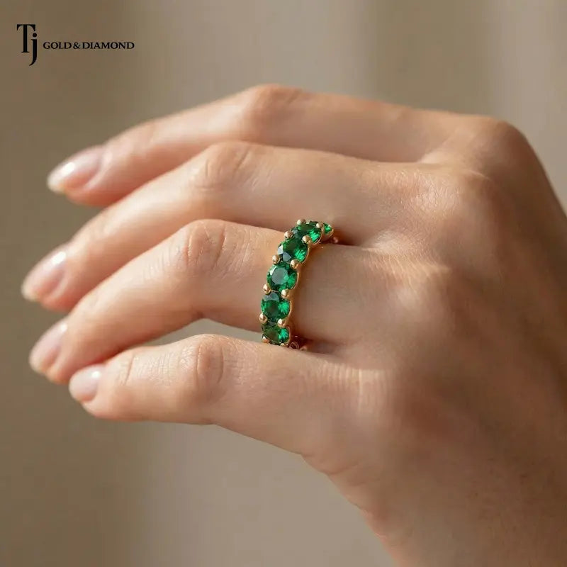 Created emerald full eternity ring in 18kt yellow gold with 1.5mm round brilliant lab-created emeralds worn on a hand.