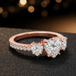 Side view of a heart cut three-stone lab-grown diamond engagement ring in 18kt rose gold with diamond shoulders