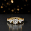 Front view of a heart cut three-stone lab-grown diamond engagement ring in 18kt yellow gold with diamond shoulders