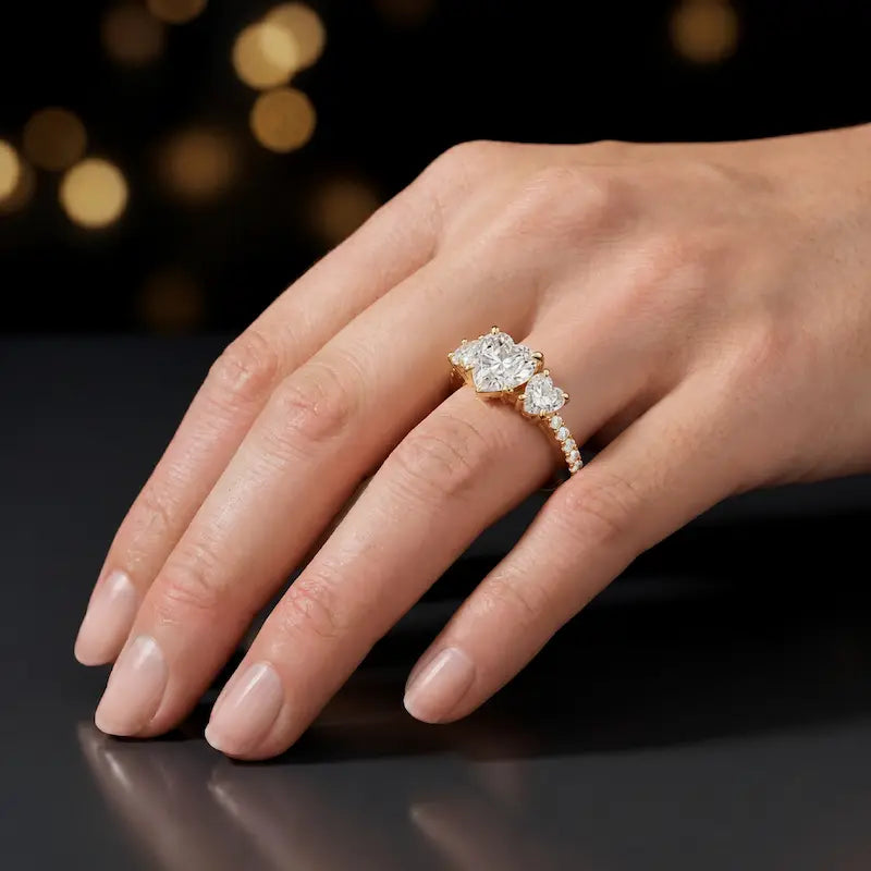 Heart cut three-stone lab-grown diamond engagement ring in 18kt yellow gold with diamond shoulders worn on hand
