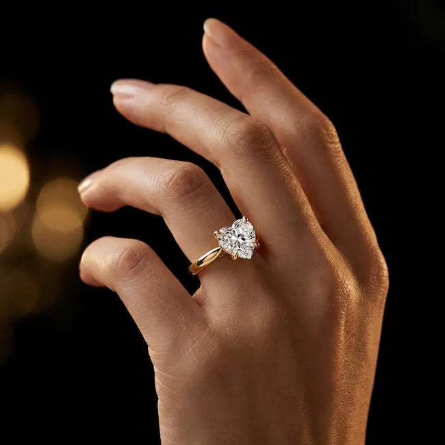 1.5 carat heart cut diamond solitaire engagement ring in an 18kt yellow gold 4 claw setting worn on a hand, by TJ Diamond