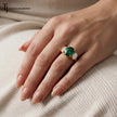 An oval lab-created emerald and diamond trilogy engagement ring in 18kt yellow gold worn on hand
