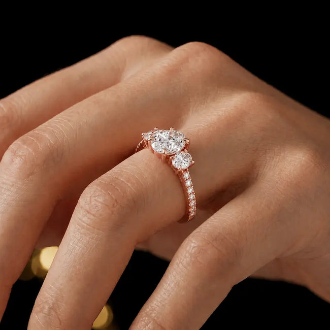 Oval cut three-stone lab-grown diamond engagement ring in 18kt rose gold with diamond shoulders worn on hand 