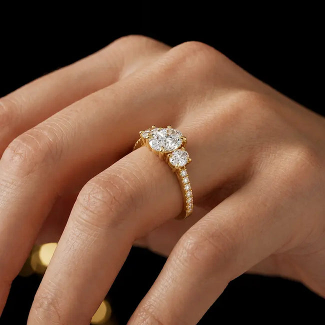 Oval cut three-stone lab-grown diamond engagement ring in 18kt yellow gold with diamond shoulders worn on hand